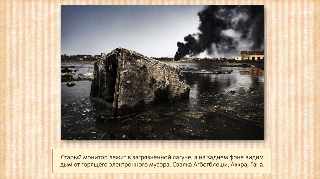 Старый монитор лежит в загрязненной лагуне, а на заднем фоне видим дым от горящего электронного мусора. Свалка Агбогблоши,